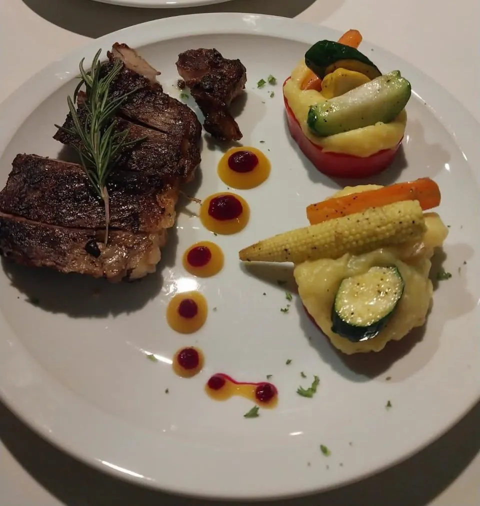 Grilled steak plated with roasted vegetables and sauce, prepared by Chef Jorge